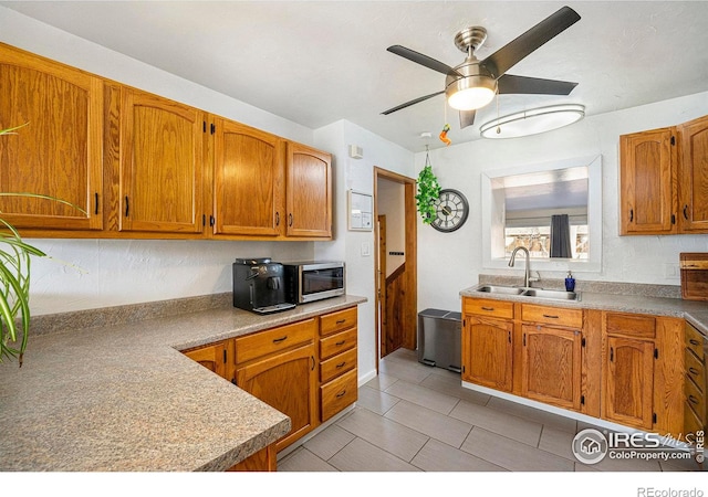 kitchen with stainless steel microwave, a sink, brown cabinetry, and a ceiling fan