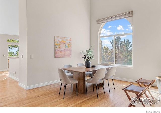 dining area with a towering ceiling and light hardwood / wood-style flooring