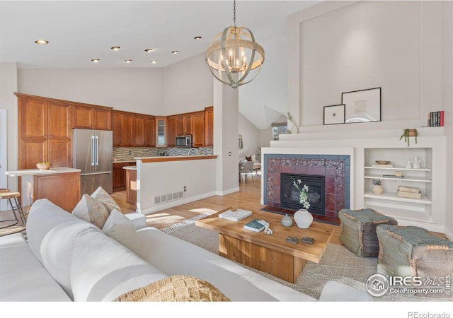 living room with built in shelves, a chandelier, high vaulted ceiling, light wood-type flooring, and a tiled fireplace