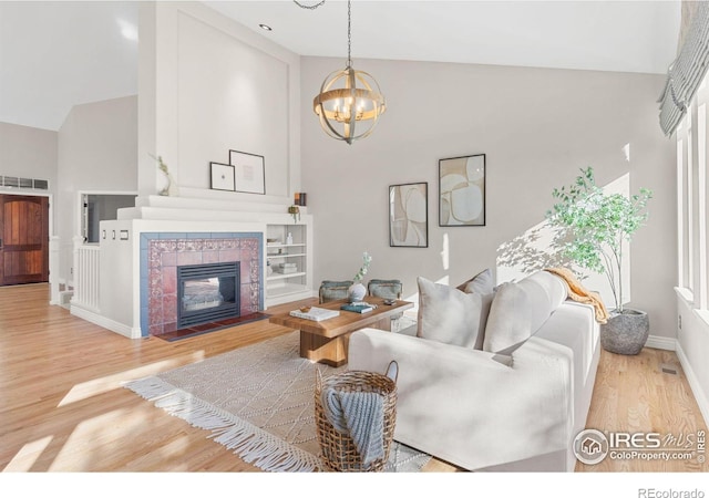 living room featuring wood-type flooring, high vaulted ceiling, a chandelier, and a fireplace