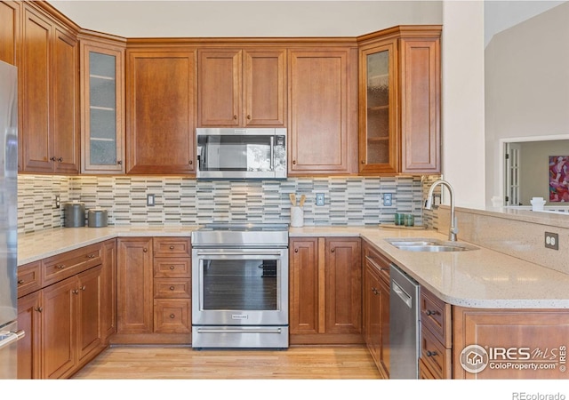 kitchen with appliances with stainless steel finishes, sink, backsplash, and light stone counters