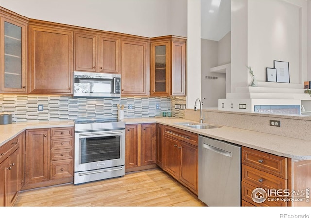 kitchen with sink, appliances with stainless steel finishes, light stone countertops, light hardwood / wood-style floors, and decorative backsplash