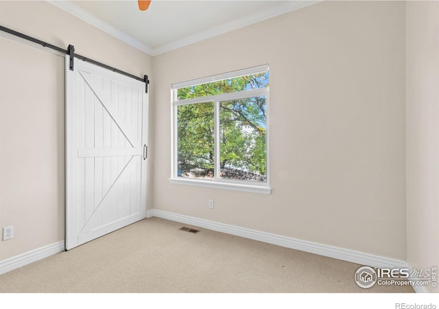 unfurnished bedroom featuring ornamental molding, a barn door, light carpet, and ceiling fan