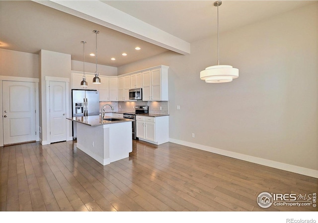 kitchen with appliances with stainless steel finishes, pendant lighting, white cabinetry, an island with sink, and sink