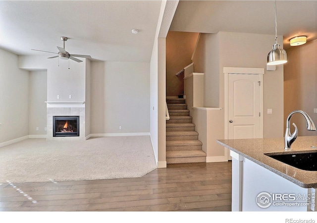 kitchen featuring sink, a tile fireplace, ceiling fan, light stone countertops, and decorative light fixtures