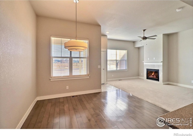 unfurnished living room with hardwood / wood-style floors, a tile fireplace, and ceiling fan