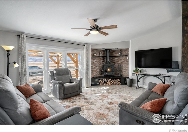 living room featuring light wood-type flooring, ceiling fan, and a wood stove