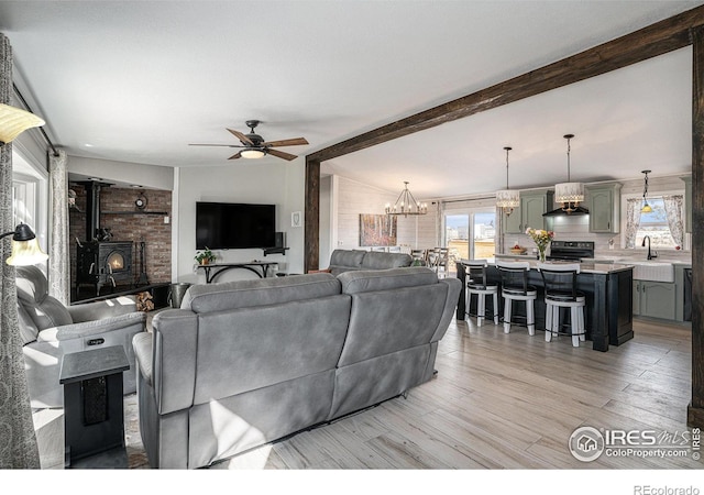 living room with sink, vaulted ceiling with beams, a wood stove, light hardwood / wood-style floors, and ceiling fan with notable chandelier