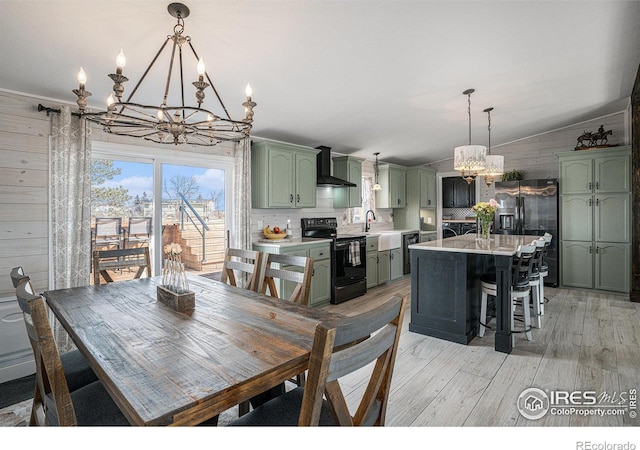 dining room featuring wood walls, lofted ceiling, sink, light wood-type flooring, and an inviting chandelier