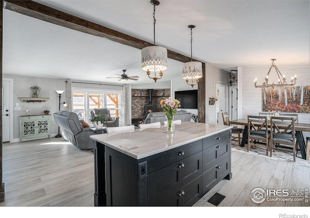 kitchen featuring ceiling fan with notable chandelier, a center island, light hardwood / wood-style floors, decorative light fixtures, and a wood stove