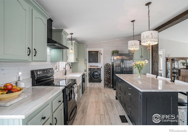 kitchen with wall chimney exhaust hood, black electric range oven, vaulted ceiling, stainless steel fridge, and washer / clothes dryer