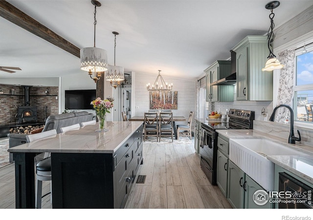 kitchen with a kitchen island, a wood stove, sink, hanging light fixtures, and electric range