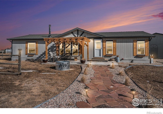 back house at dusk featuring a pergola and a patio