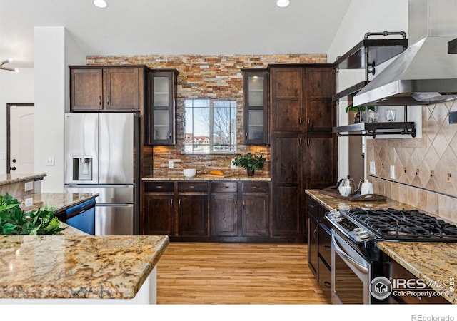 kitchen with stainless steel appliances, light stone counters, extractor fan, tasteful backsplash, and light hardwood / wood-style floors