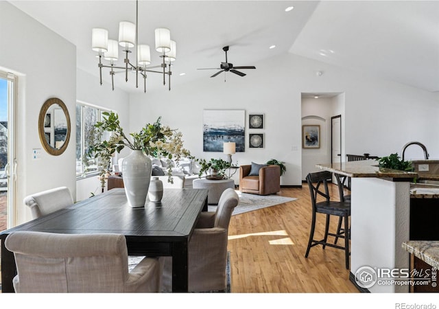 dining area with lofted ceiling, ceiling fan with notable chandelier, and light hardwood / wood-style floors