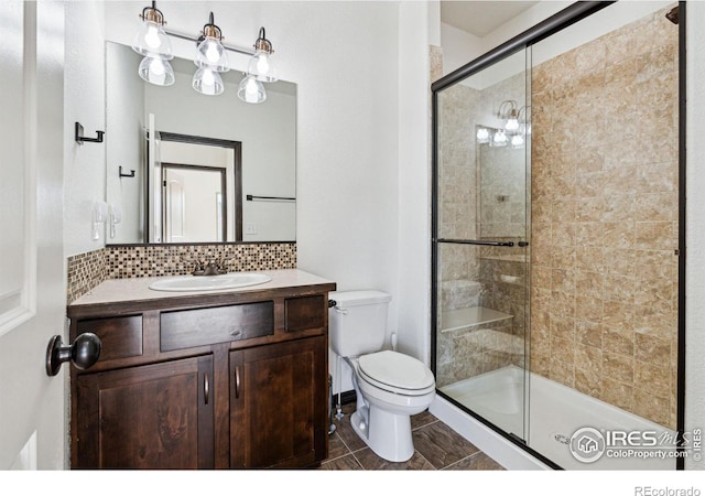 bathroom featuring vanity, backsplash, a shower with door, and toilet