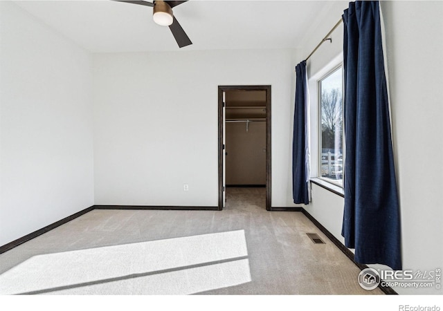 unfurnished bedroom with a walk in closet, light colored carpet, and ceiling fan