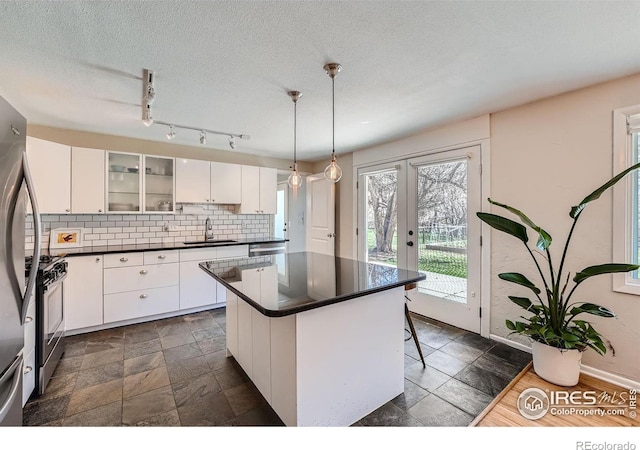 kitchen featuring a kitchen island, pendant lighting, white cabinetry, sink, and stainless steel gas range oven