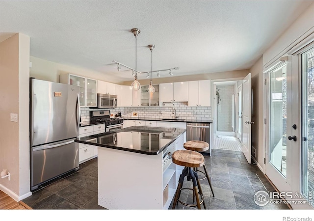 kitchen featuring sink, appliances with stainless steel finishes, white cabinetry, a center island, and decorative light fixtures