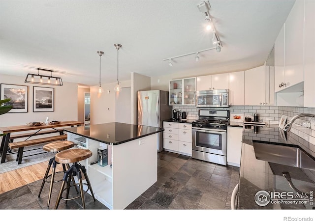 kitchen with appliances with stainless steel finishes, white cabinetry, a center island, decorative backsplash, and decorative light fixtures