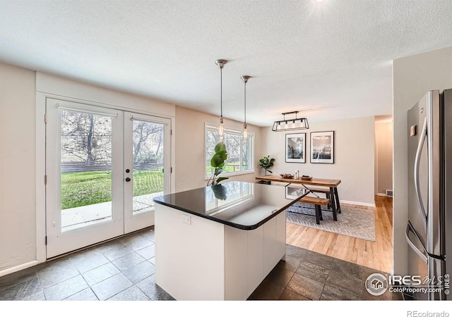 kitchen featuring hanging light fixtures, white cabinetry, stainless steel fridge, and a textured ceiling