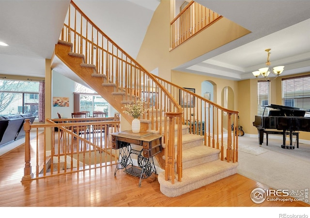 stairway with hardwood / wood-style floors, an inviting chandelier, and a tray ceiling