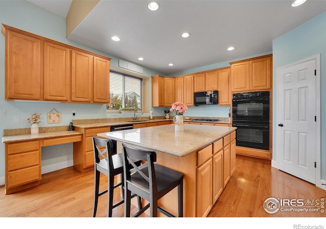 kitchen featuring a breakfast bar area, a center island, light hardwood / wood-style floors, black appliances, and light stone countertops