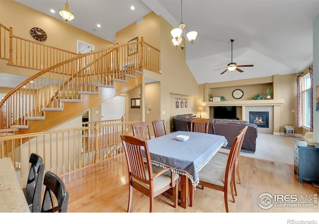 dining area with high vaulted ceiling, ceiling fan with notable chandelier, and light hardwood / wood-style floors