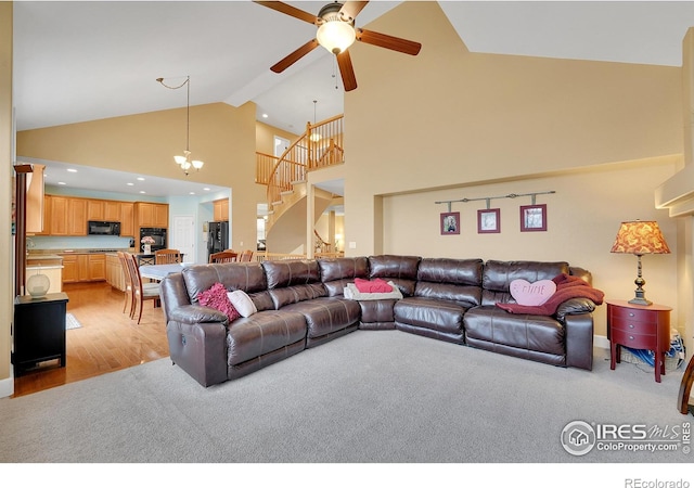 carpeted living room featuring ceiling fan with notable chandelier and high vaulted ceiling