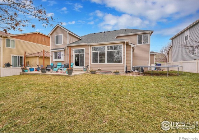 rear view of house featuring a trampoline, a patio area, and a lawn