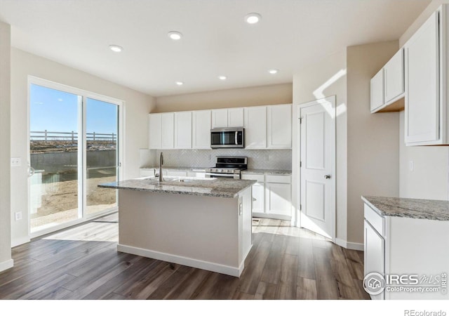 kitchen with white cabinetry, light stone counters, stainless steel appliances, and an island with sink