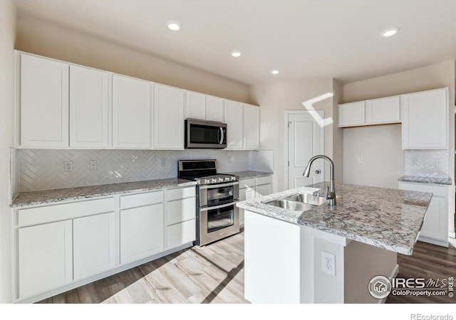 kitchen with white cabinetry, appliances with stainless steel finishes, sink, and a center island with sink