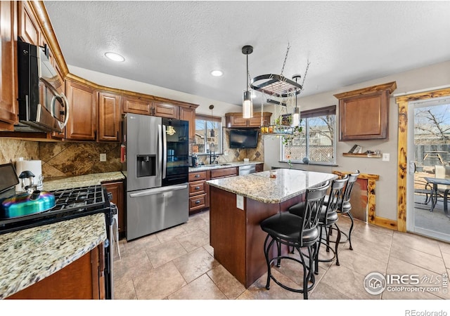 kitchen featuring light stone counters, tasteful backsplash, a center island, appliances with stainless steel finishes, and a kitchen breakfast bar