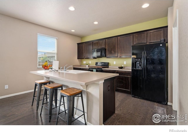 kitchen with sink, dark brown cabinets, a center island with sink, a kitchen breakfast bar, and black appliances