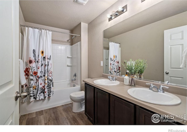 full bathroom with wood-type flooring, vanity, toilet, shower / bathtub combination with curtain, and a textured ceiling