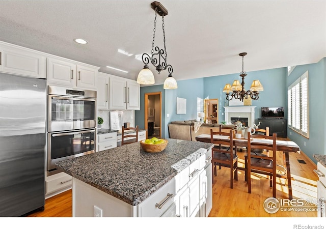 kitchen featuring appliances with stainless steel finishes, a center island, white cabinets, and decorative light fixtures