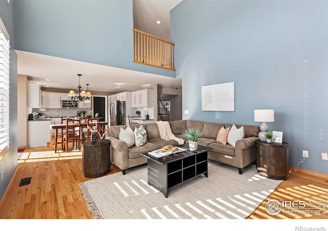 living room with an inviting chandelier, a towering ceiling, and light hardwood / wood-style flooring