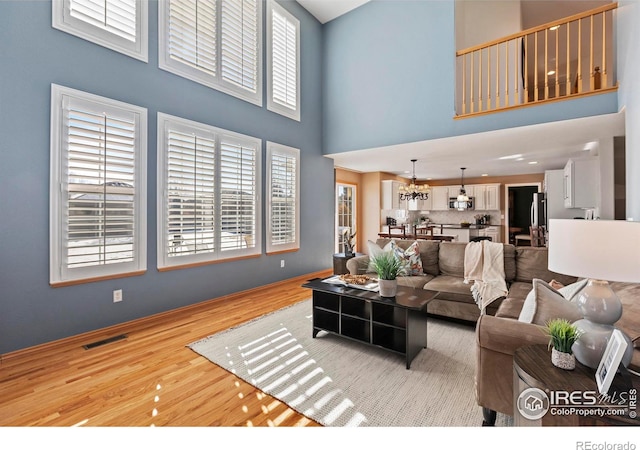 living room with a high ceiling, plenty of natural light, a notable chandelier, and light hardwood / wood-style flooring