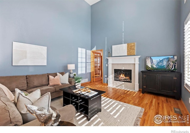 living room featuring wood-type flooring, a towering ceiling, and a fireplace