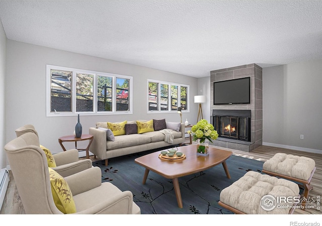 living room featuring hardwood / wood-style flooring, a tile fireplace, a textured ceiling, and a baseboard radiator