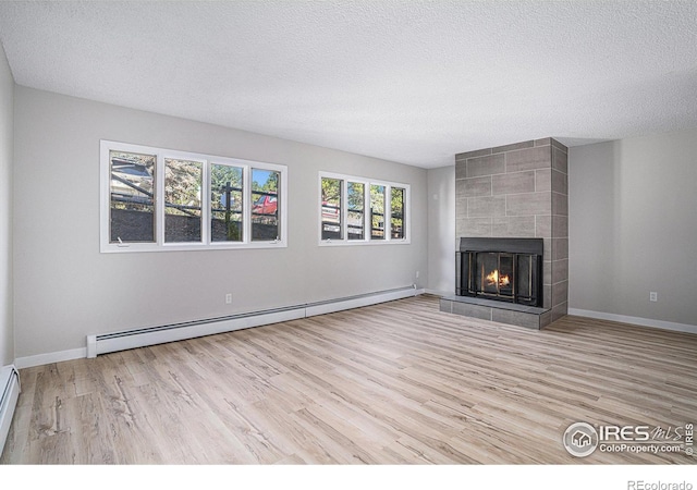 unfurnished living room with a tile fireplace, a baseboard heating unit, a textured ceiling, and light hardwood / wood-style flooring