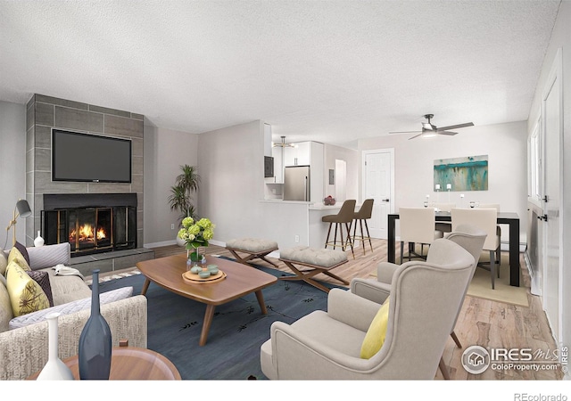 living room with a tiled fireplace, ceiling fan, light hardwood / wood-style flooring, and a textured ceiling