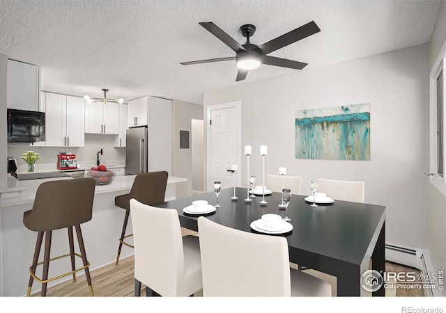 dining area with a baseboard heating unit, sink, a textured ceiling, and light hardwood / wood-style flooring