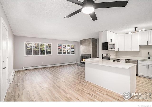 kitchen featuring white cabinetry, sink, a tiled fireplace, baseboard heating, and stainless steel appliances