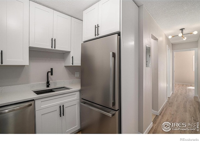 kitchen with sink, a textured ceiling, stainless steel appliances, light hardwood / wood-style floors, and white cabinets