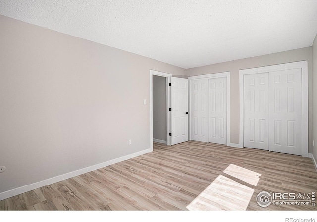 unfurnished bedroom featuring multiple closets, light hardwood / wood-style floors, and a textured ceiling