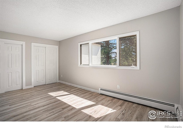 unfurnished bedroom with light wood-type flooring, two closets, a textured ceiling, and baseboard heating