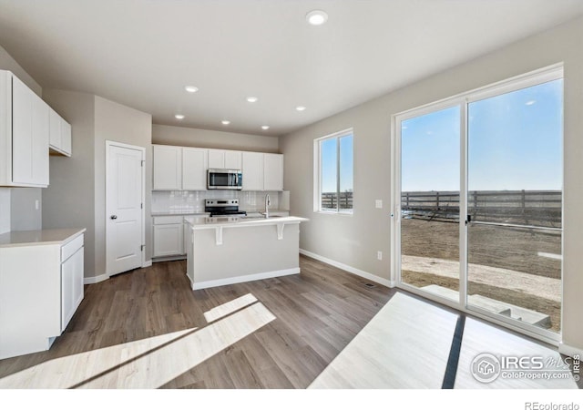 kitchen featuring light hardwood / wood-style flooring, appliances with stainless steel finishes, white cabinets, a center island with sink, and decorative backsplash