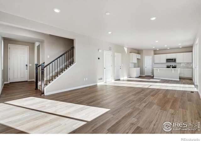 unfurnished living room with stairs, light wood-style floors, baseboards, and recessed lighting