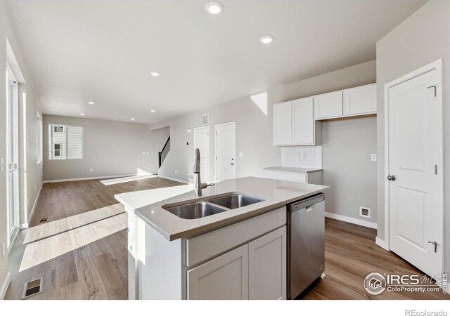kitchen featuring dishwasher, a sink, white cabinets, wood finished floors, and baseboards